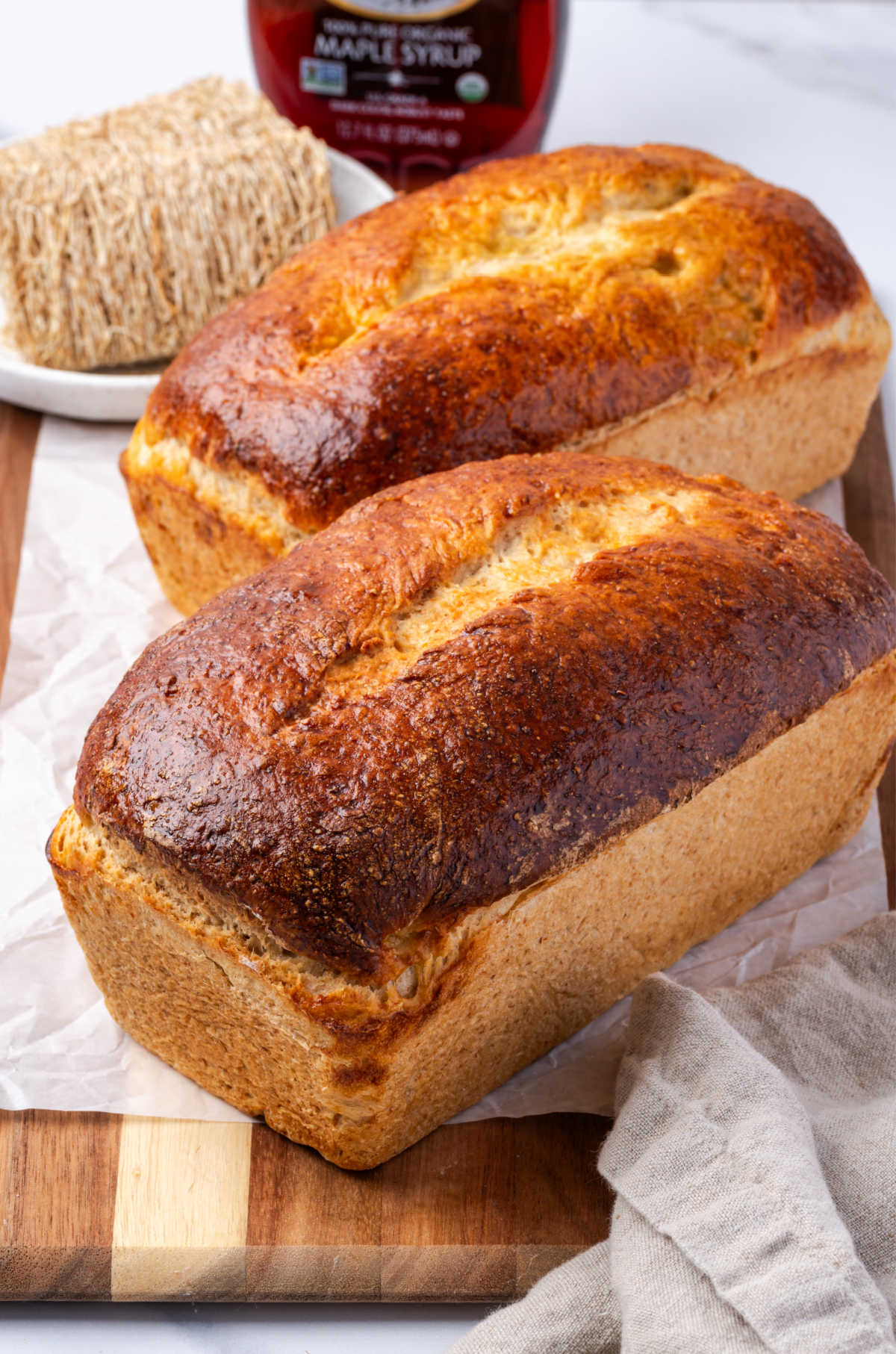 Two loaves of bread on wooden cutting board.