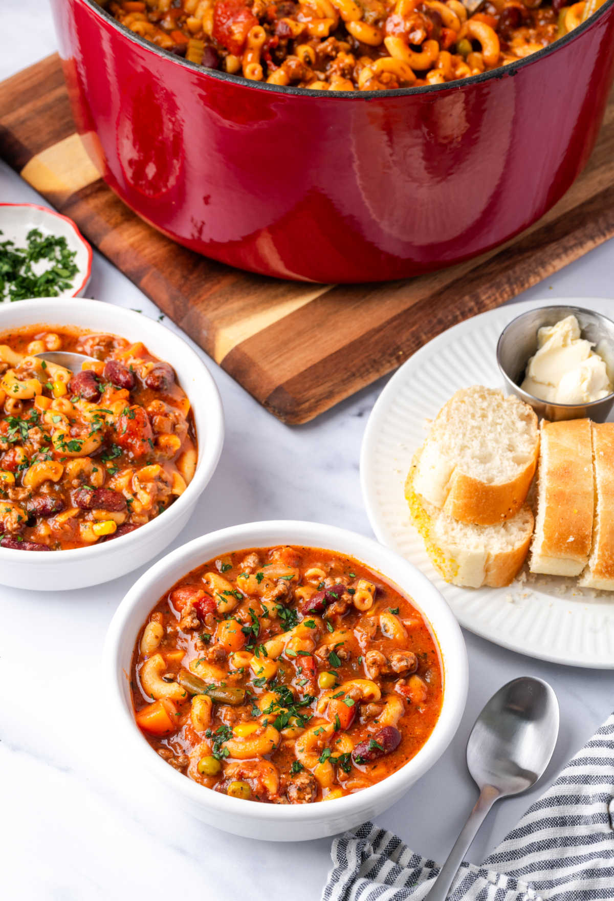 Beef vegetable soup in small white bowls with slices of bread in background.