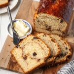Cinnamon raisin bread partially sliced on wood cutting board.