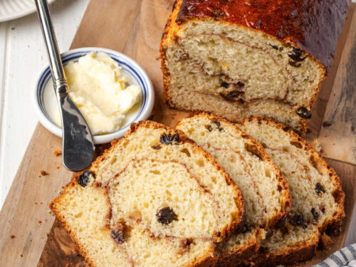 Cinnamon raisin bread partially sliced on wood cutting board.