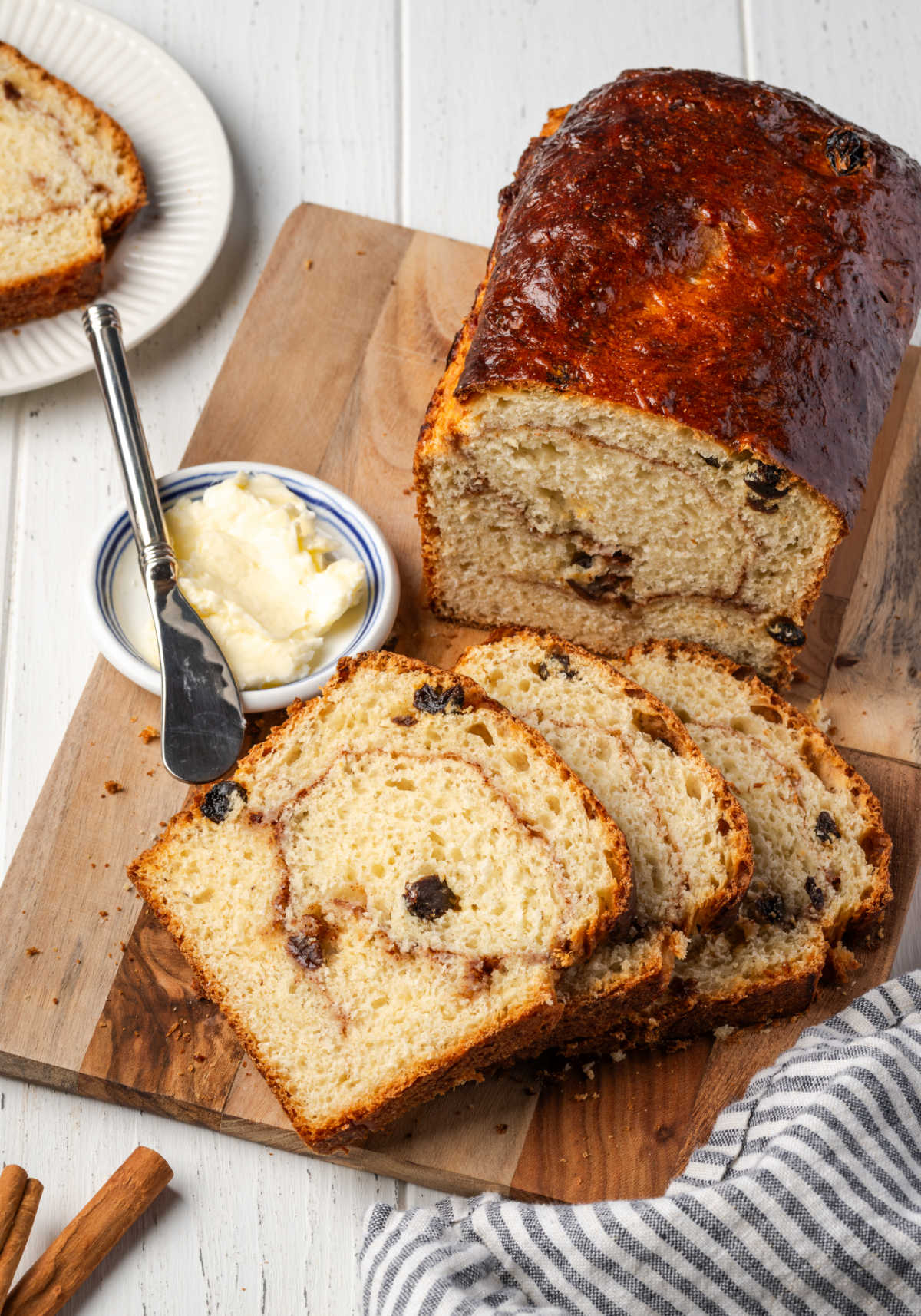Cinnamon raisin bread partially sliced on wood cutting board.