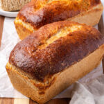 Loaves of shredded wheat bread on wood cutting board.