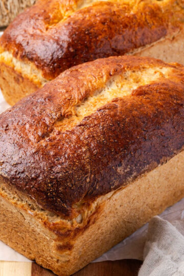 Loaves of shredded wheat bread on wood cutting board.