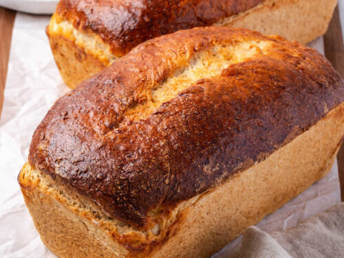 Loaves of shredded wheat bread on wood cutting board.
