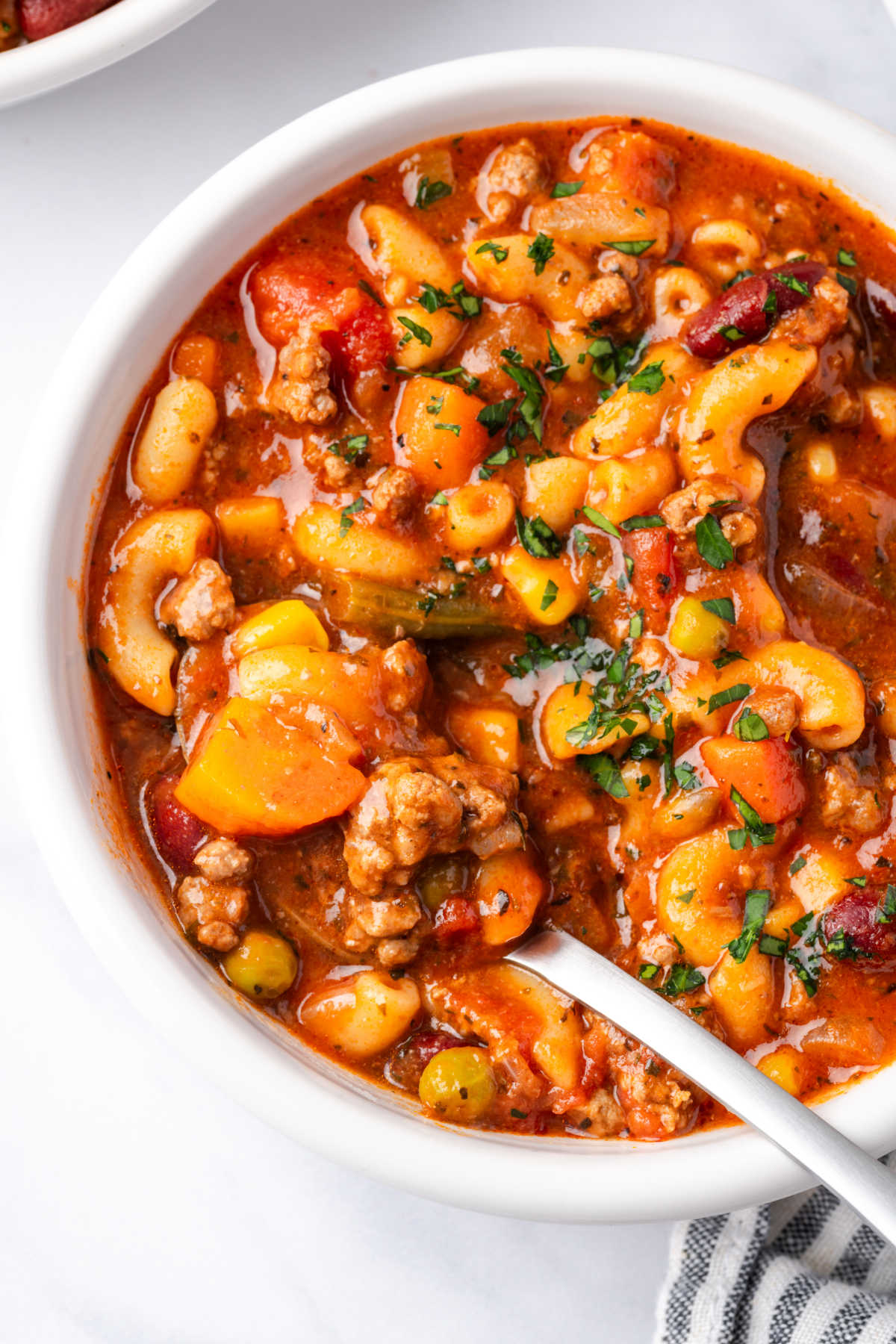 Beef soup with vegetables and elbow macaroni in small white bowl with spoon.