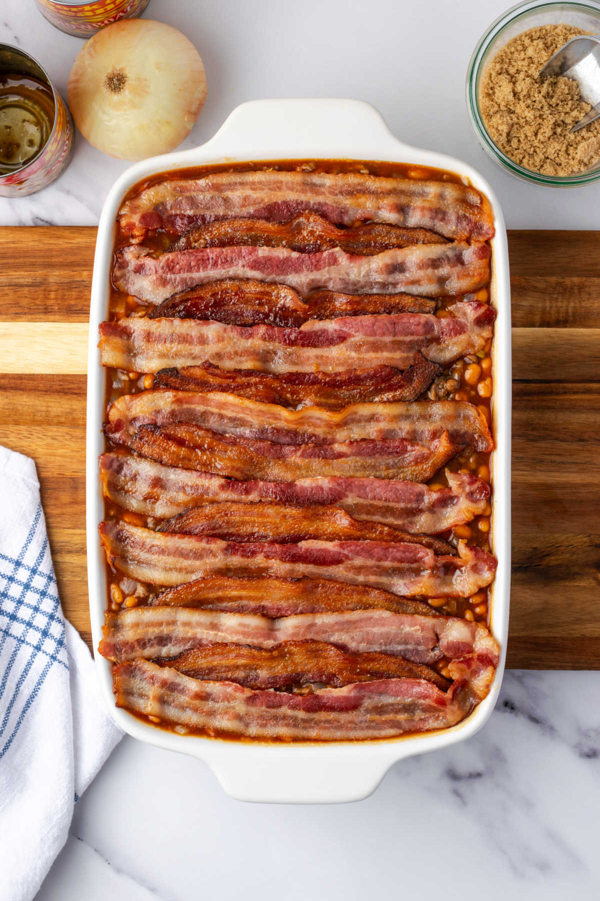 Bacon on top of baked beans in white casserole dish.