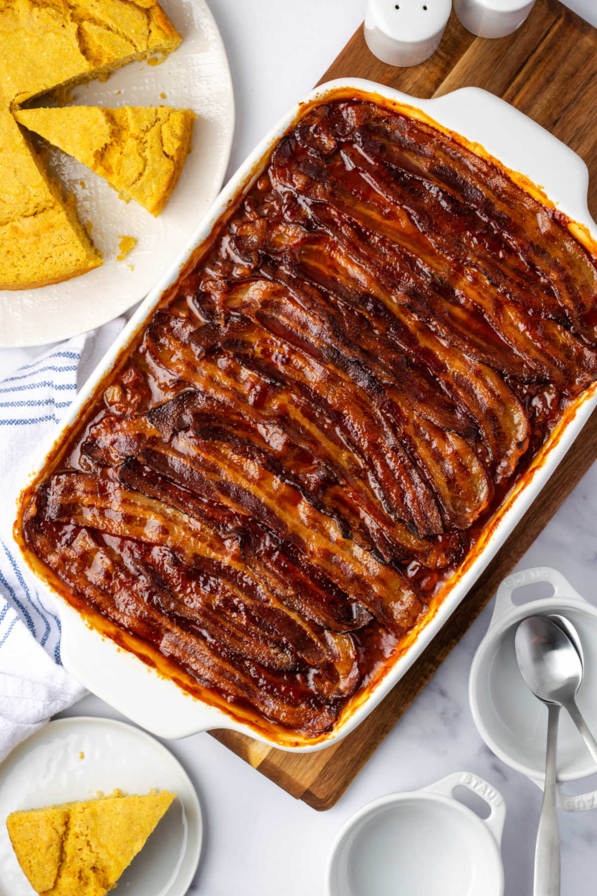 Cowboy baked beans in white casserole dish topped with bacon slices.