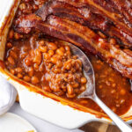 Baked beans with hamburger topped with bacon in white baking dish.
