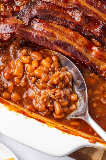 Baked beans with hamburger topped with bacon in white baking dish.