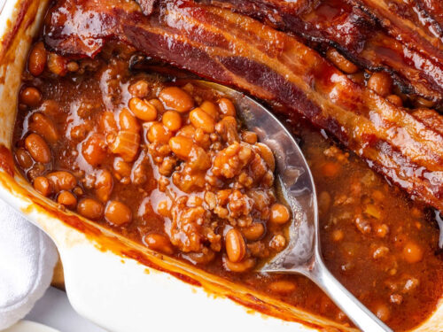 Baked beans with hamburger topped with bacon in white baking dish.