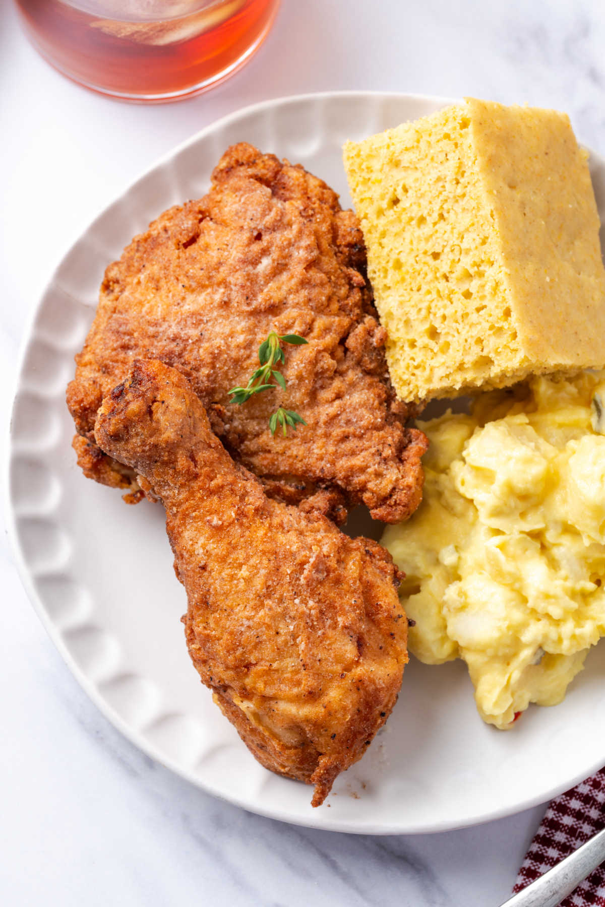Fried chicken on white plate with potato salad and cornbread.