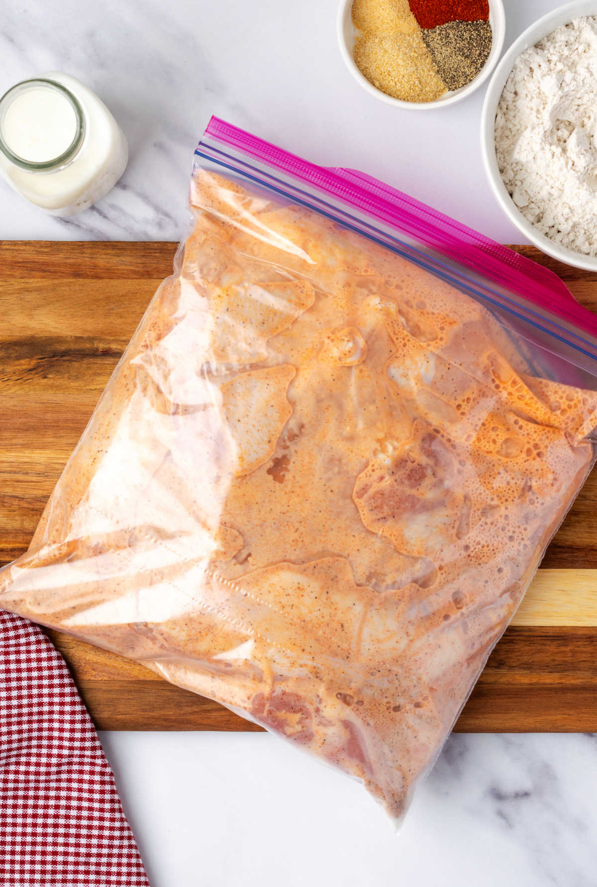 Chicken marinating in seasoned buttermilk on wood cutting board.