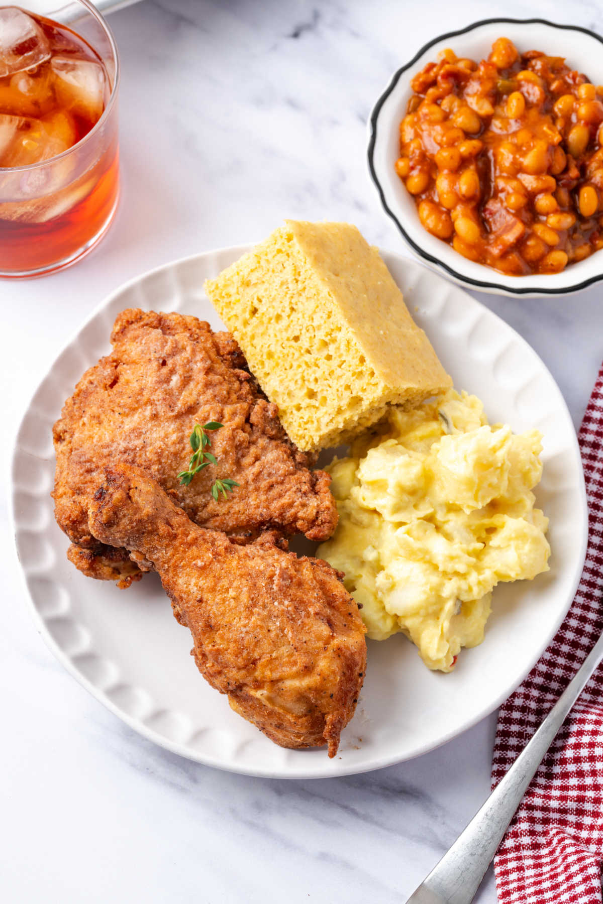 Fried chicken on white plate with potato salad, cornbread and baked beans.