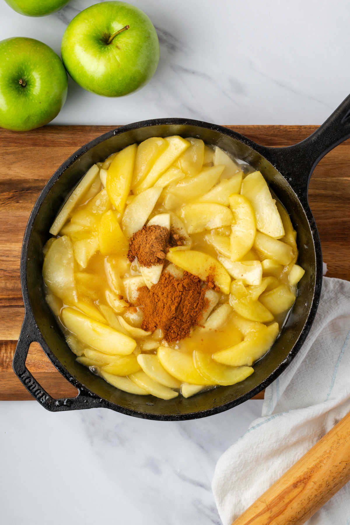 Adding cinnamon and nutmeg to cooked apples in cast iron skillet.