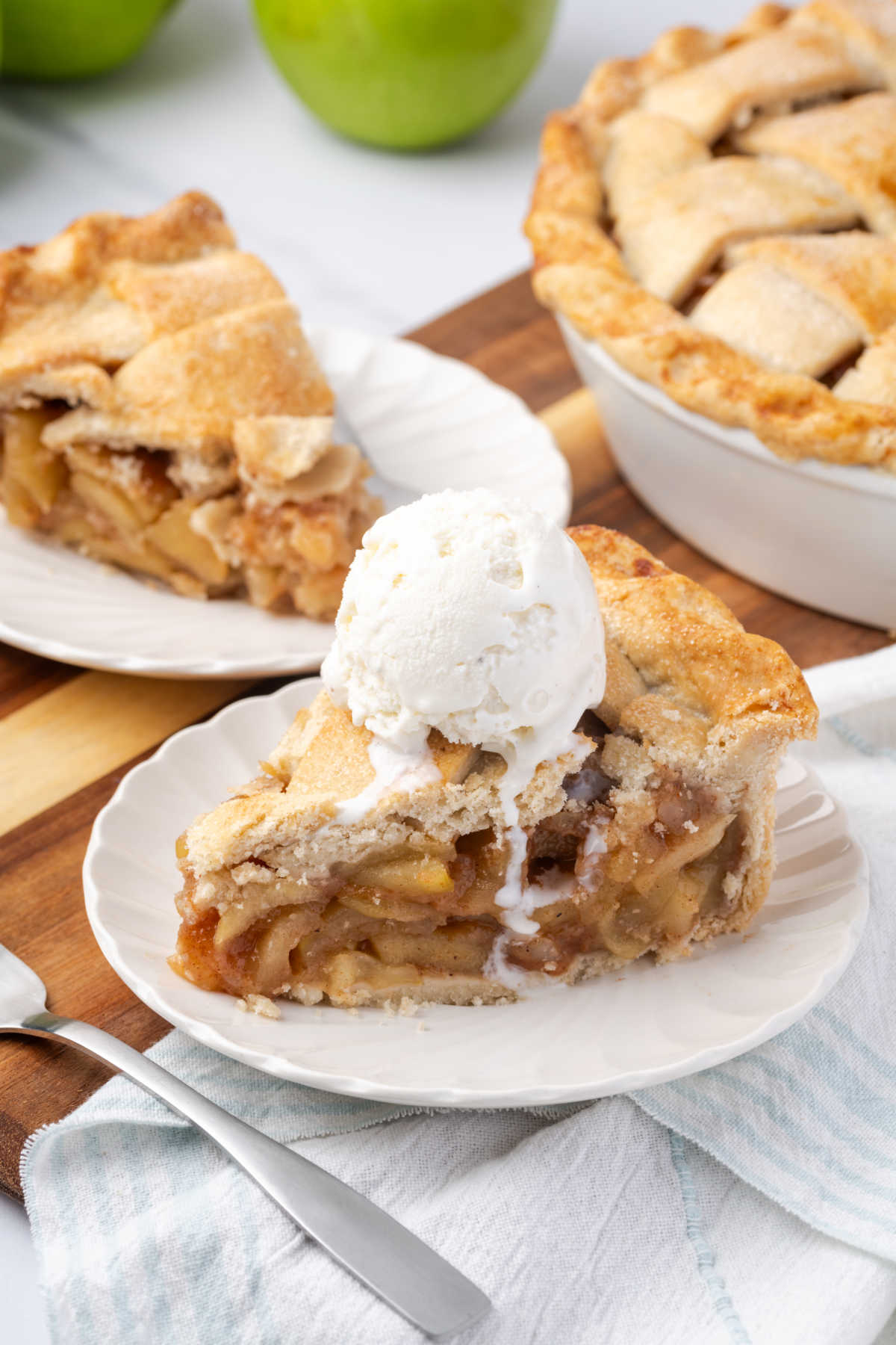 Slice of apple pie on small white plate with scoop of vanilla ice cream.
