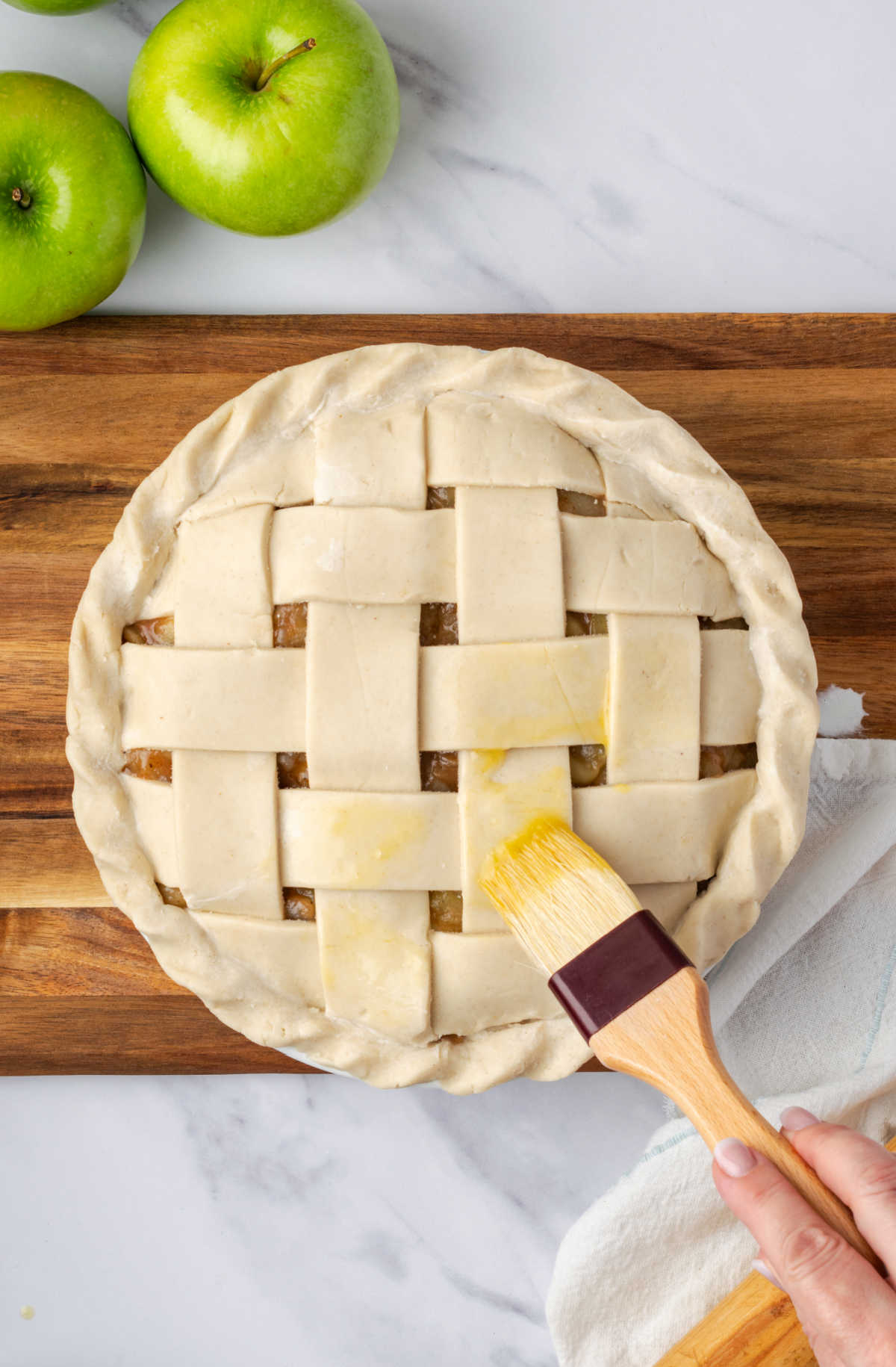 Brushing on egg wash on an unbaked pie with lattice crust.