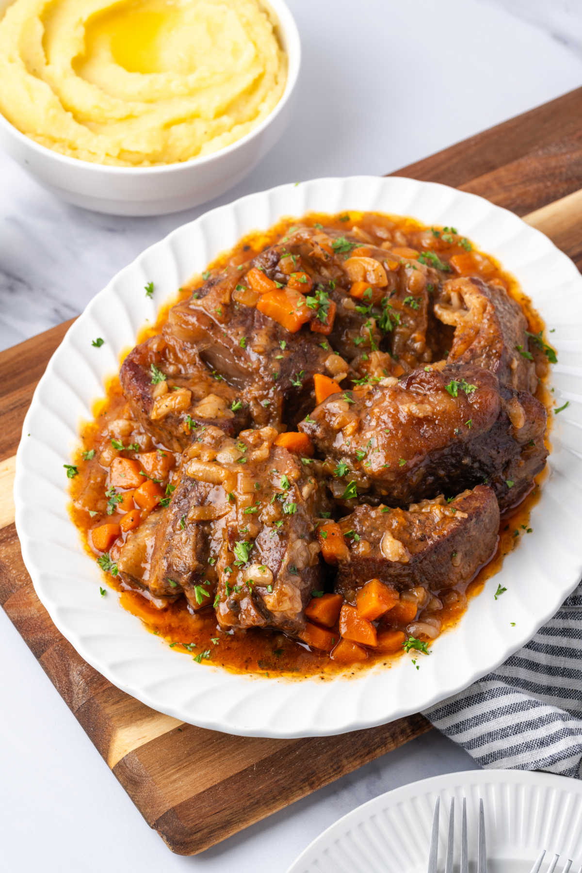 White oval plate with short ribs, onions, carrots and fresh parsley.