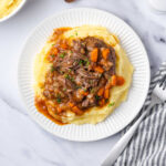 Short ribs, mashed potatoes, carrots, onions on small white plate.