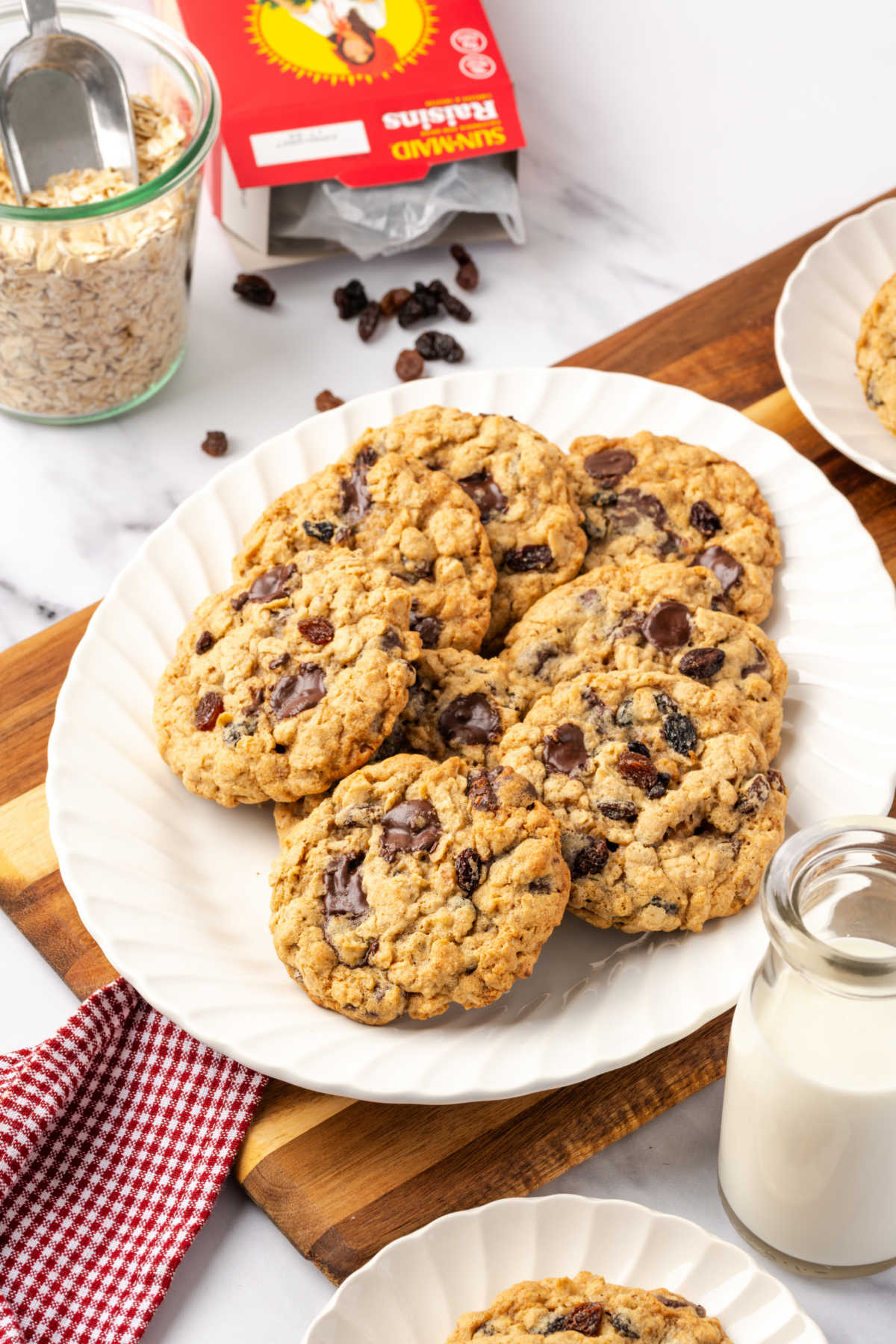Oatmeal cookies on small white plate, glass of milk to side.