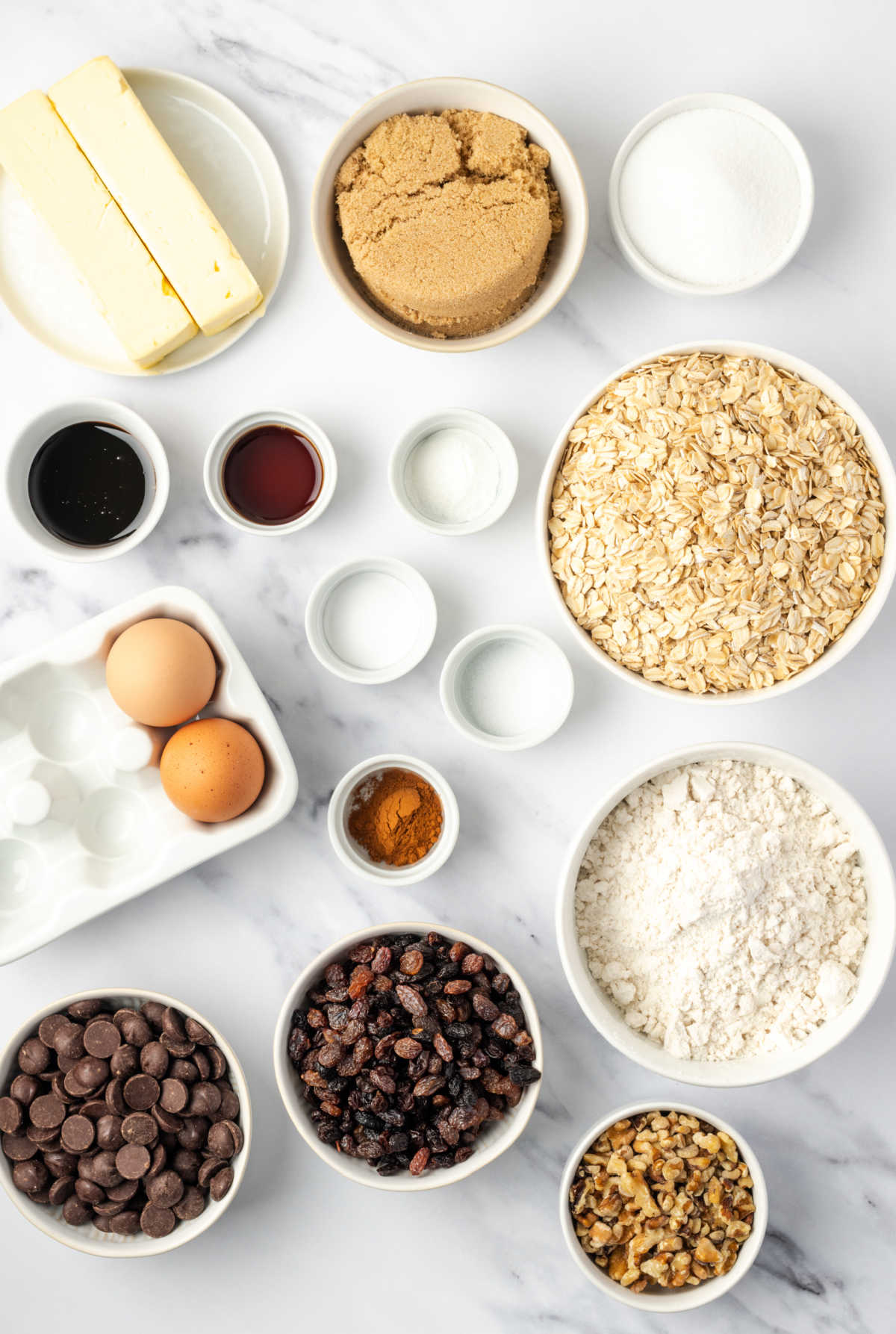 Ingredients in small white bowls on white marble for oatmeal cookies.