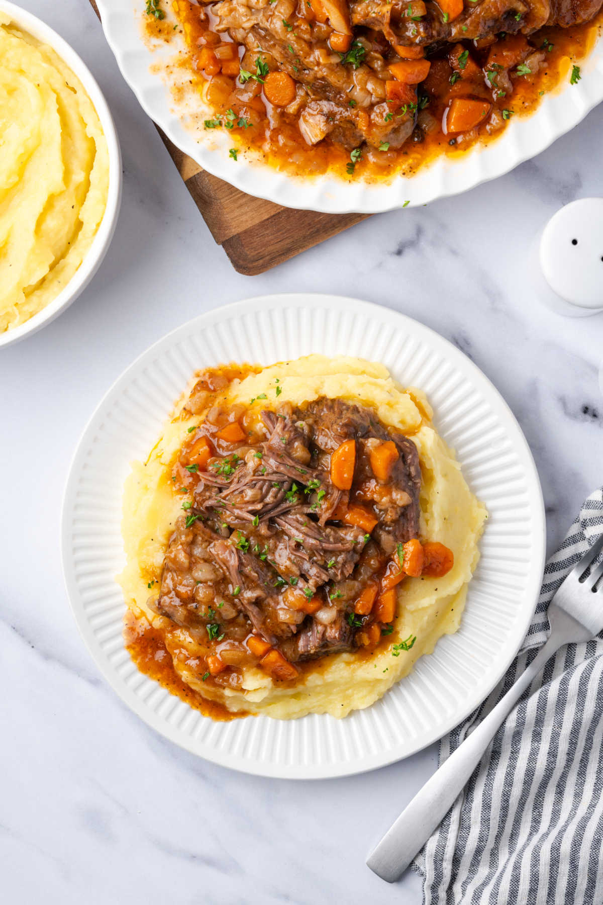 Small white plate with short ribs, mashed potatoes, carrots, onions.