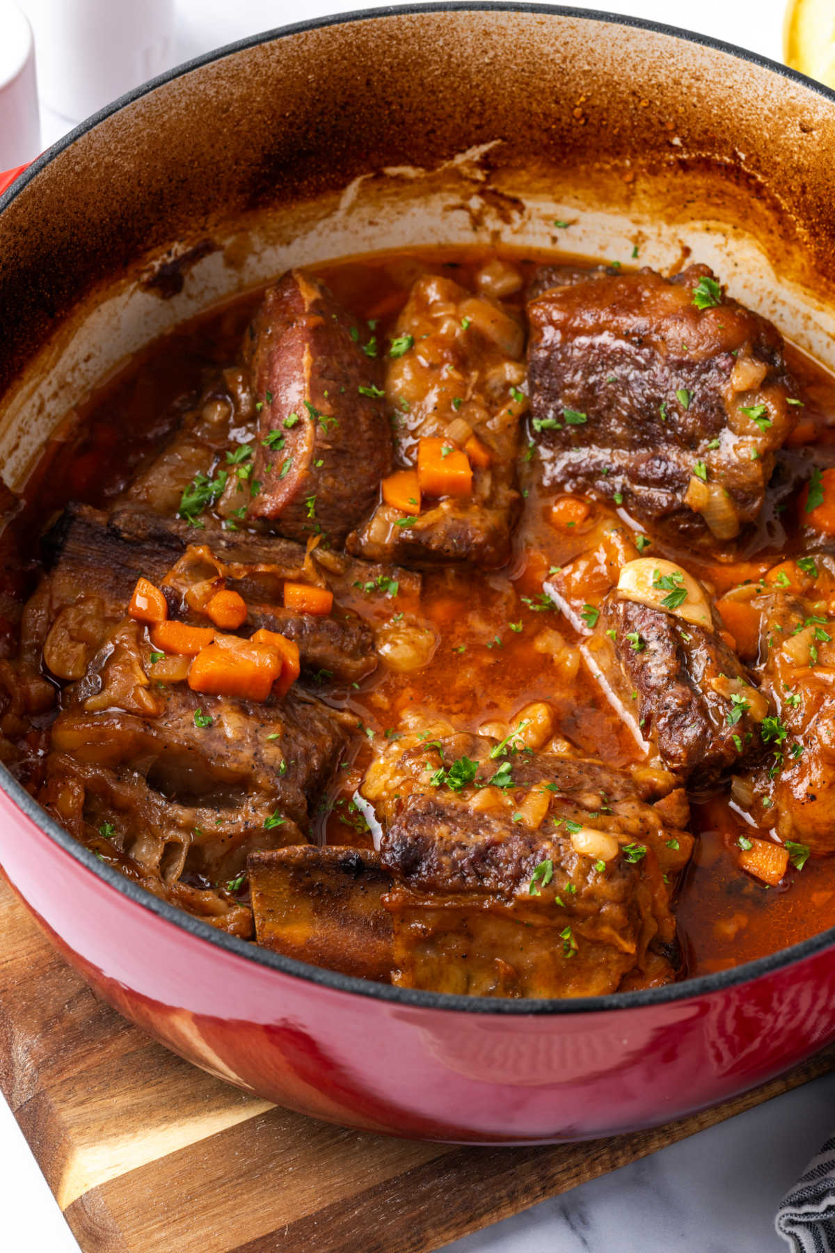 Dutch oven with short ribs, sauce, carrots, garlic, fresh parsley.