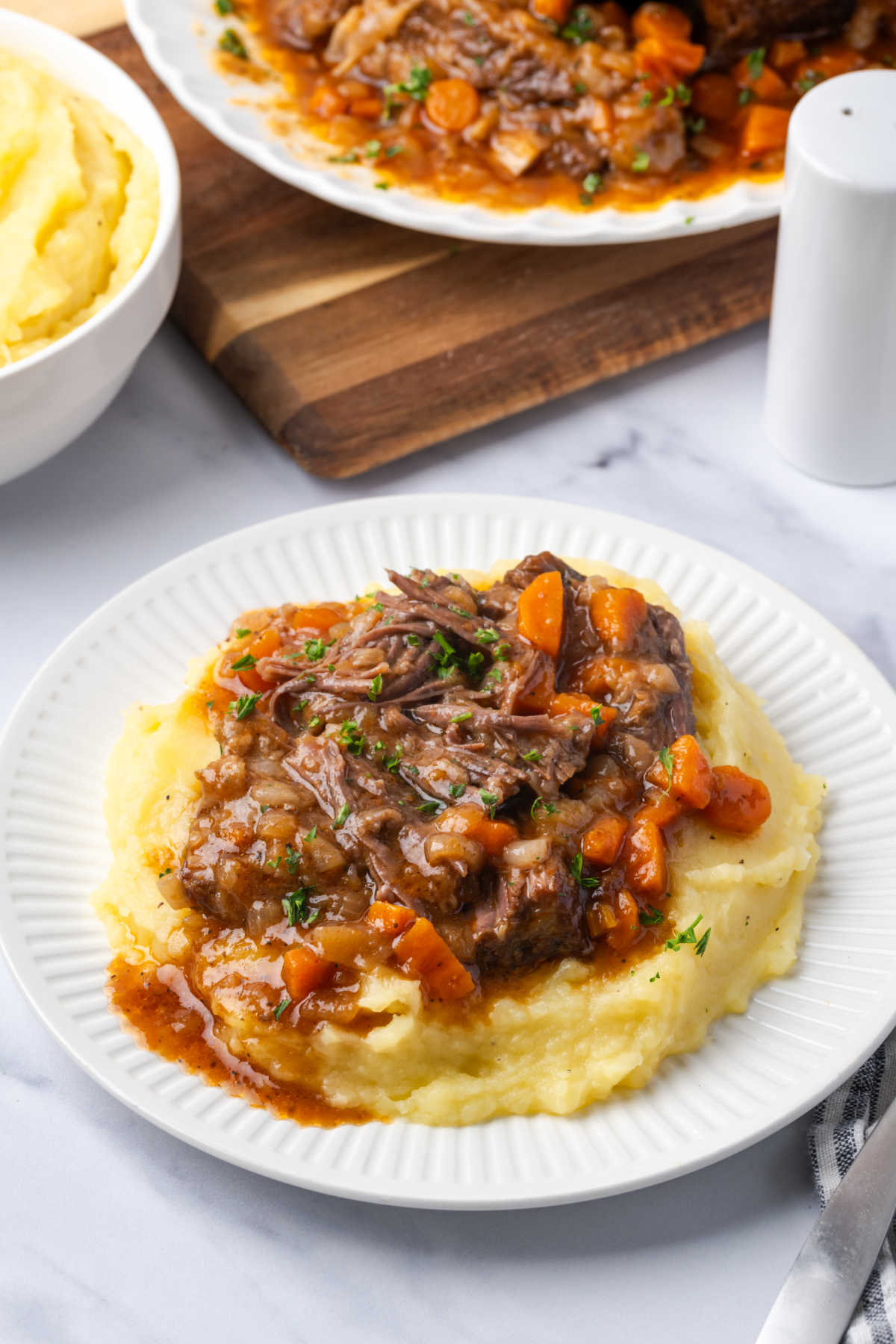 Small white plate with mashed potatoes, short ribs and carrots.