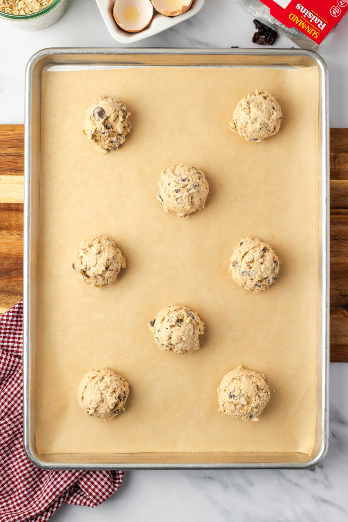 Oatmeal raisin cookie dough rounds on sheet pan before baking.