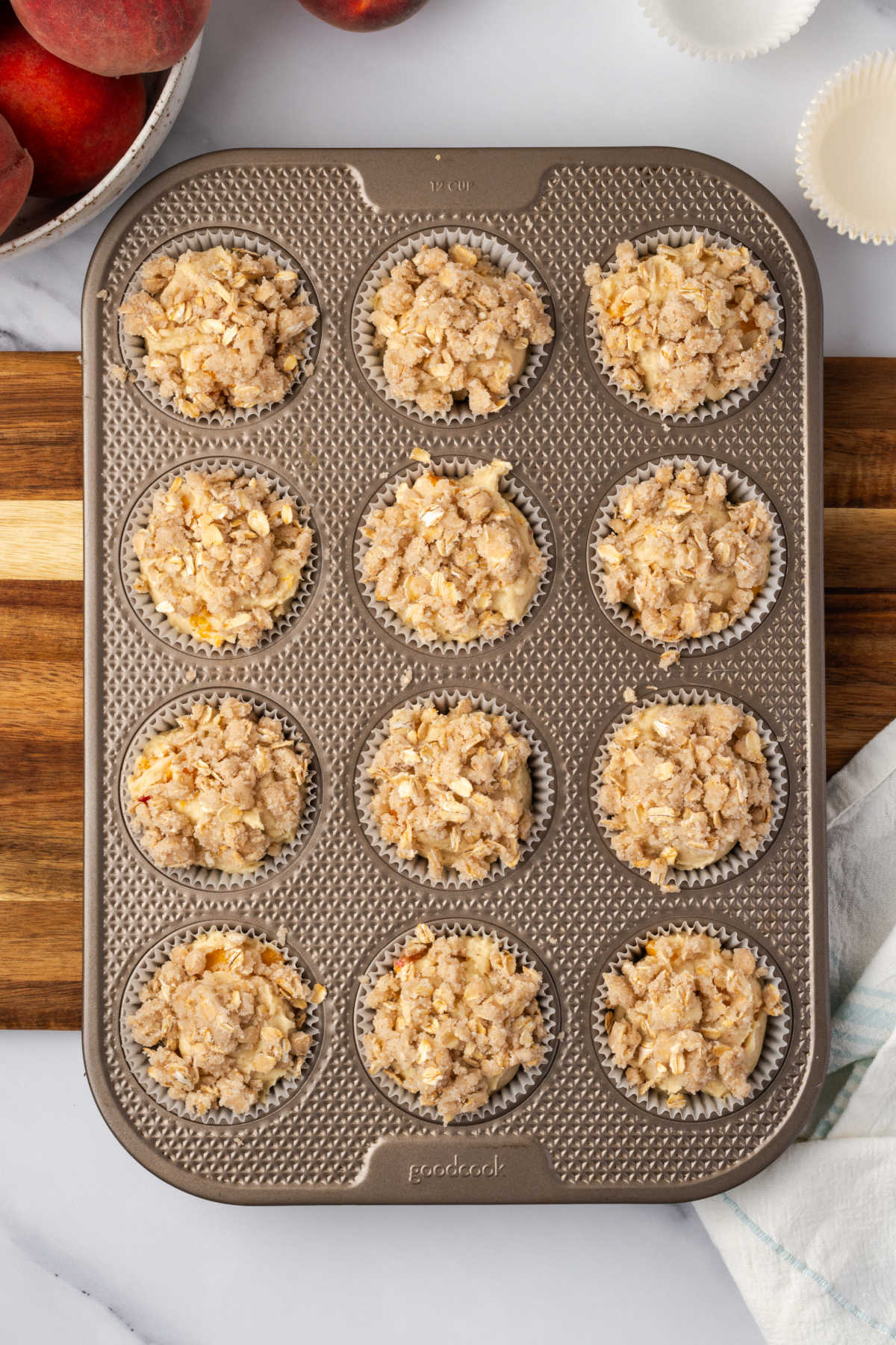 Unbaked muffins with streusel topping in metal muffin pan.