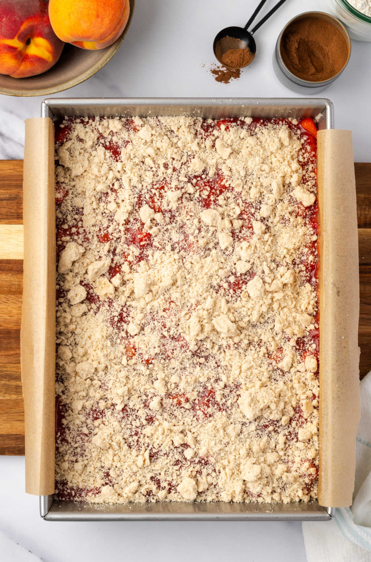 Unbaked crumb bars in rectangle baking pan, fresh peaches in background.