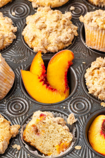 Close up of peach muffins with fresh peaches in muffin tin.