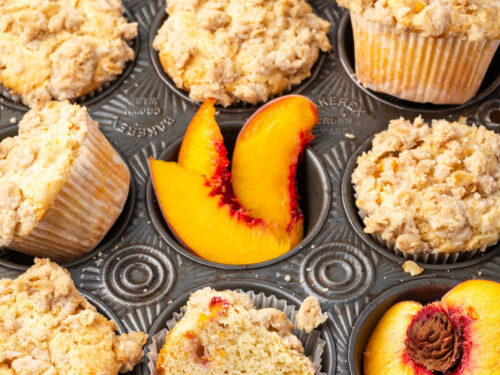 Close up of peach muffins with fresh peaches in muffin tin.