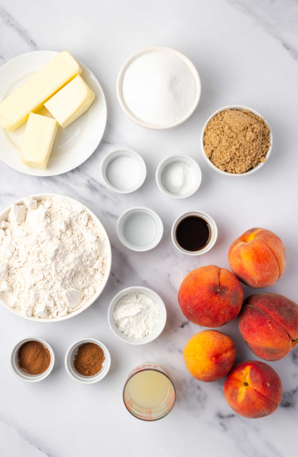 Ingredients in small white bowls for crumb bars, fresh peaches on white marble.