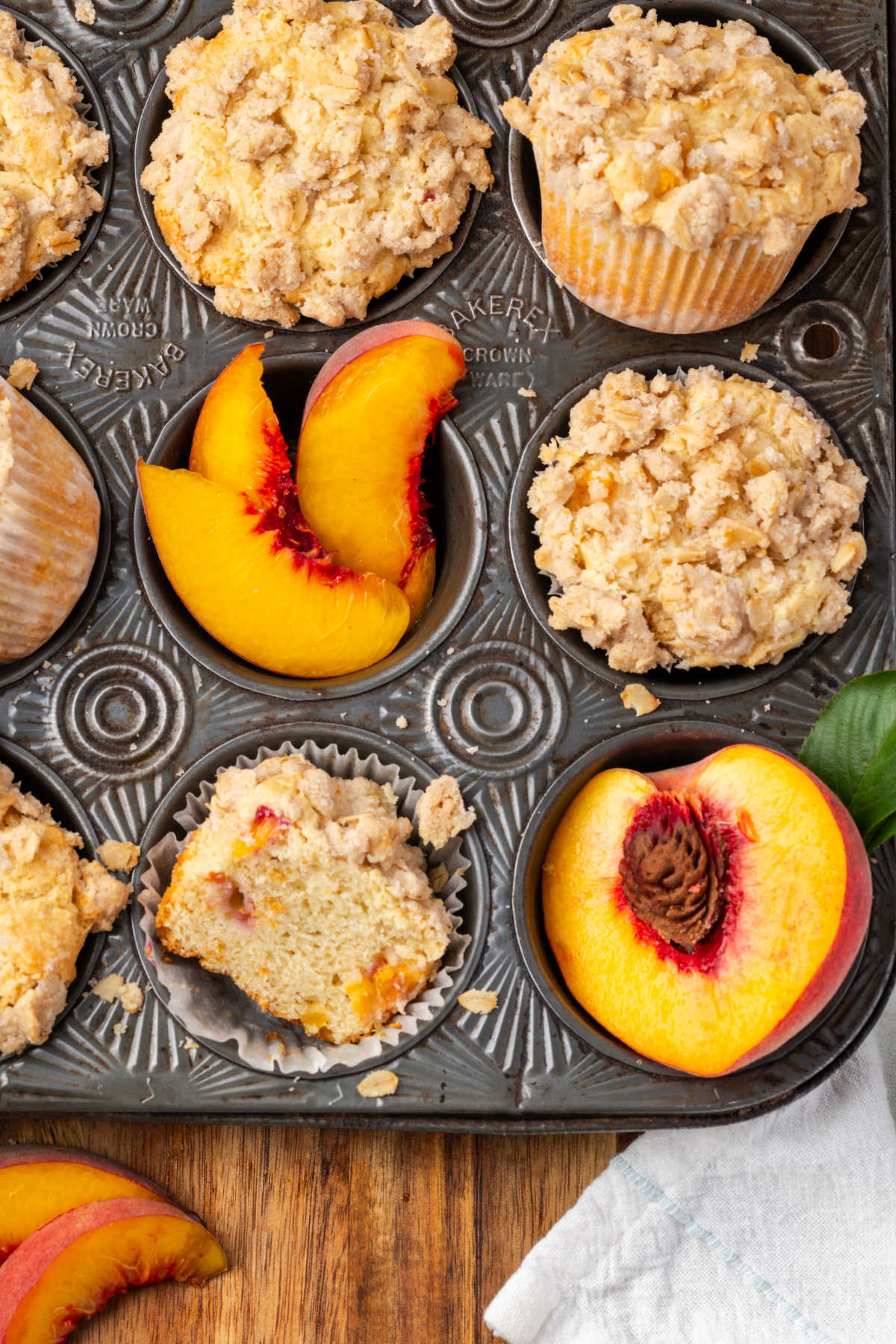 Peach muffins in vintage muffin tin, fresh peaches around.