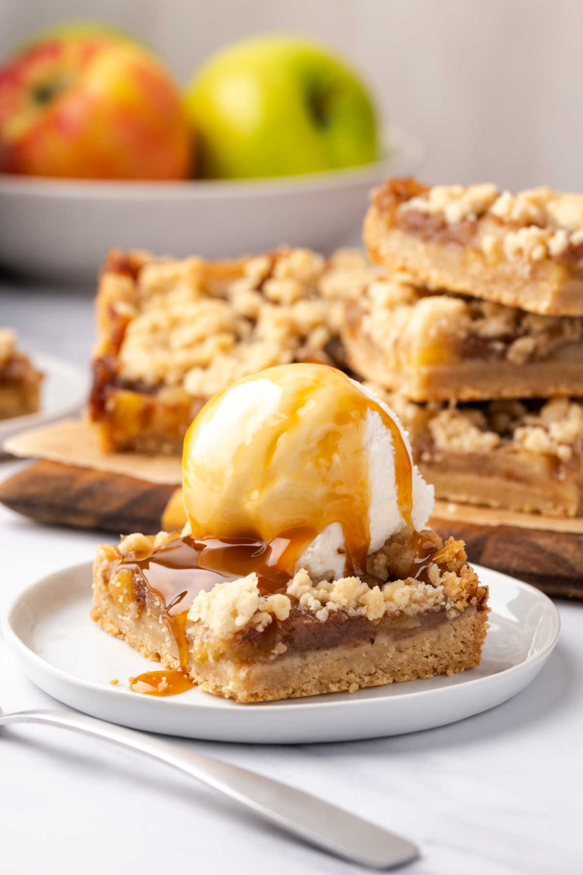 Apple crumb bar topped with scoop of ice cream on small white plate.