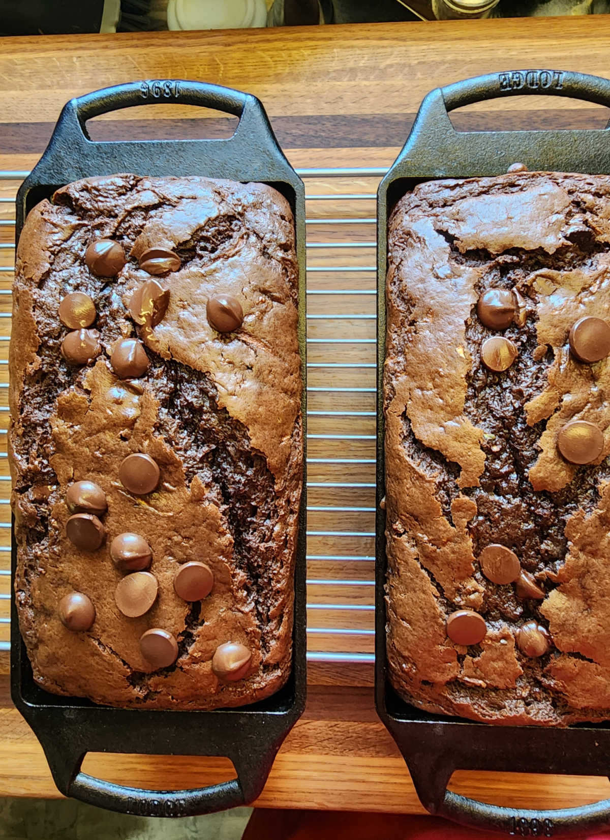 Overhead shot of two loaves of chocolate zucchini bread in cast iron loaf pans on wood cutting board.