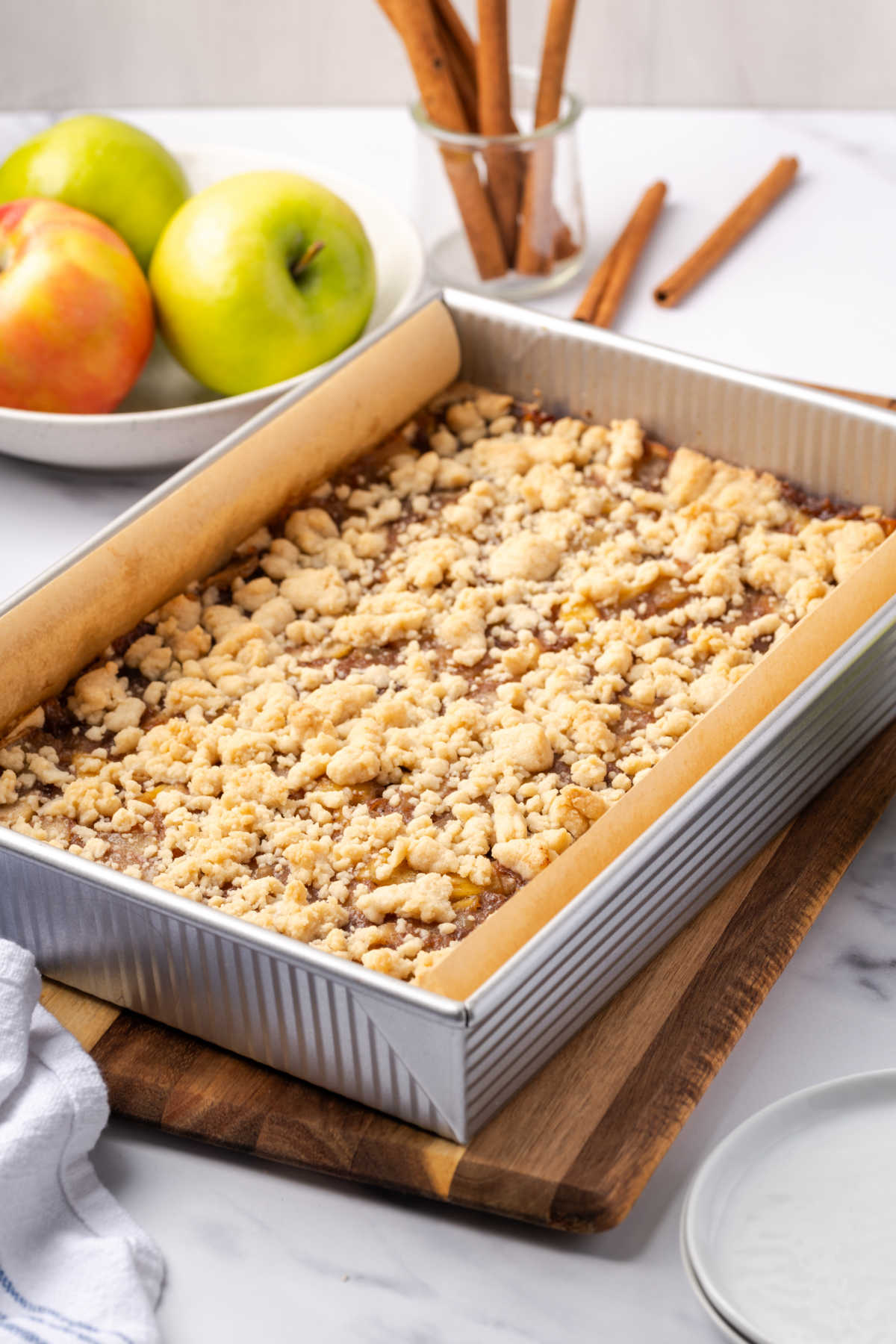 Baked apple bars in metal baking pan on wood cutting board.