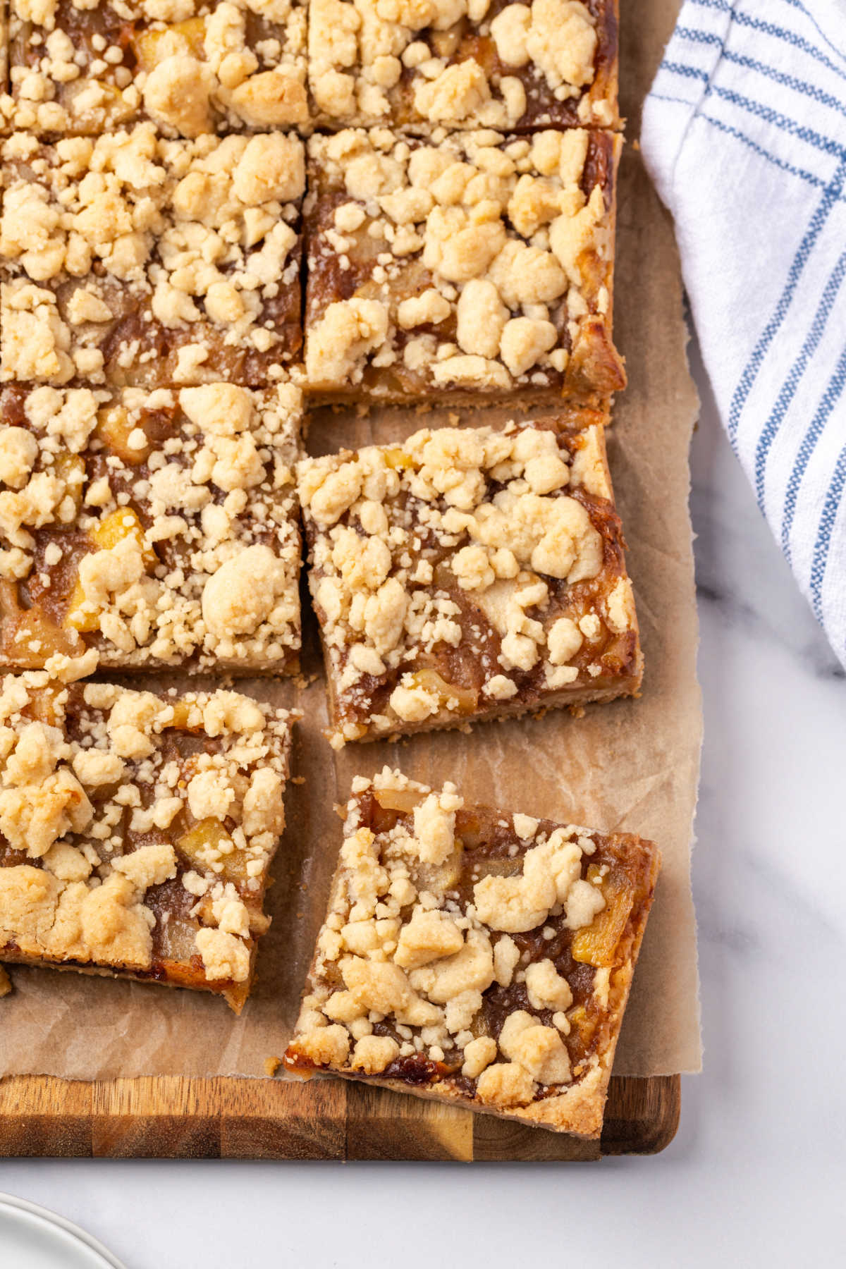 Apple crumb bars cut into squares on wood cutting board.