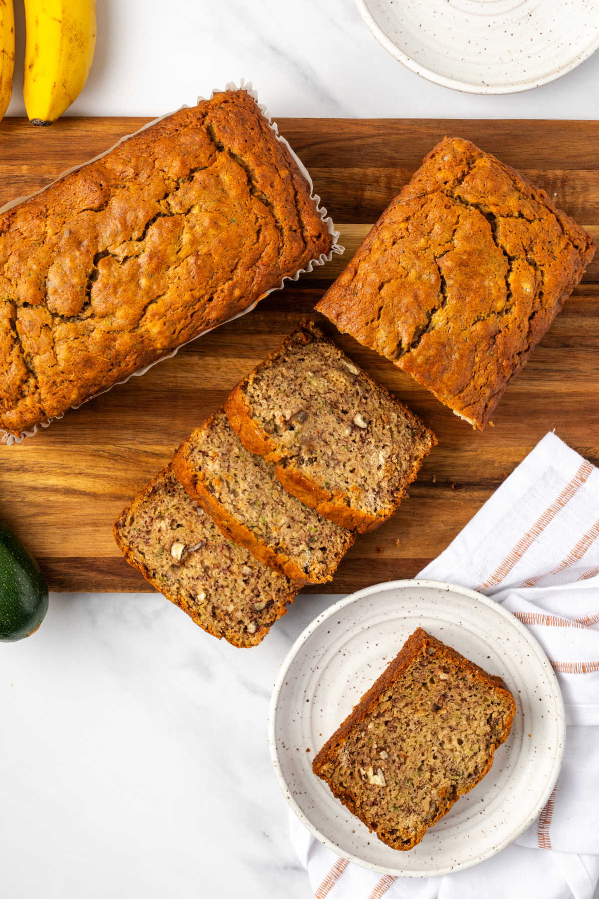 Banana zucchini bread loaves partially sliced on cutting board.