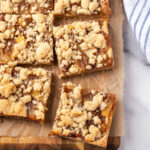 Apple bars cut into squares on wood cutting board.