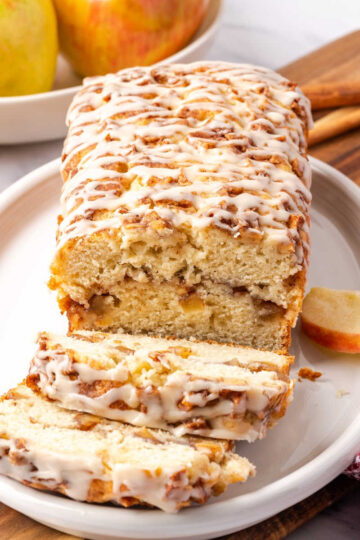 Apple fritter loaf partially sliced on white oval dish.