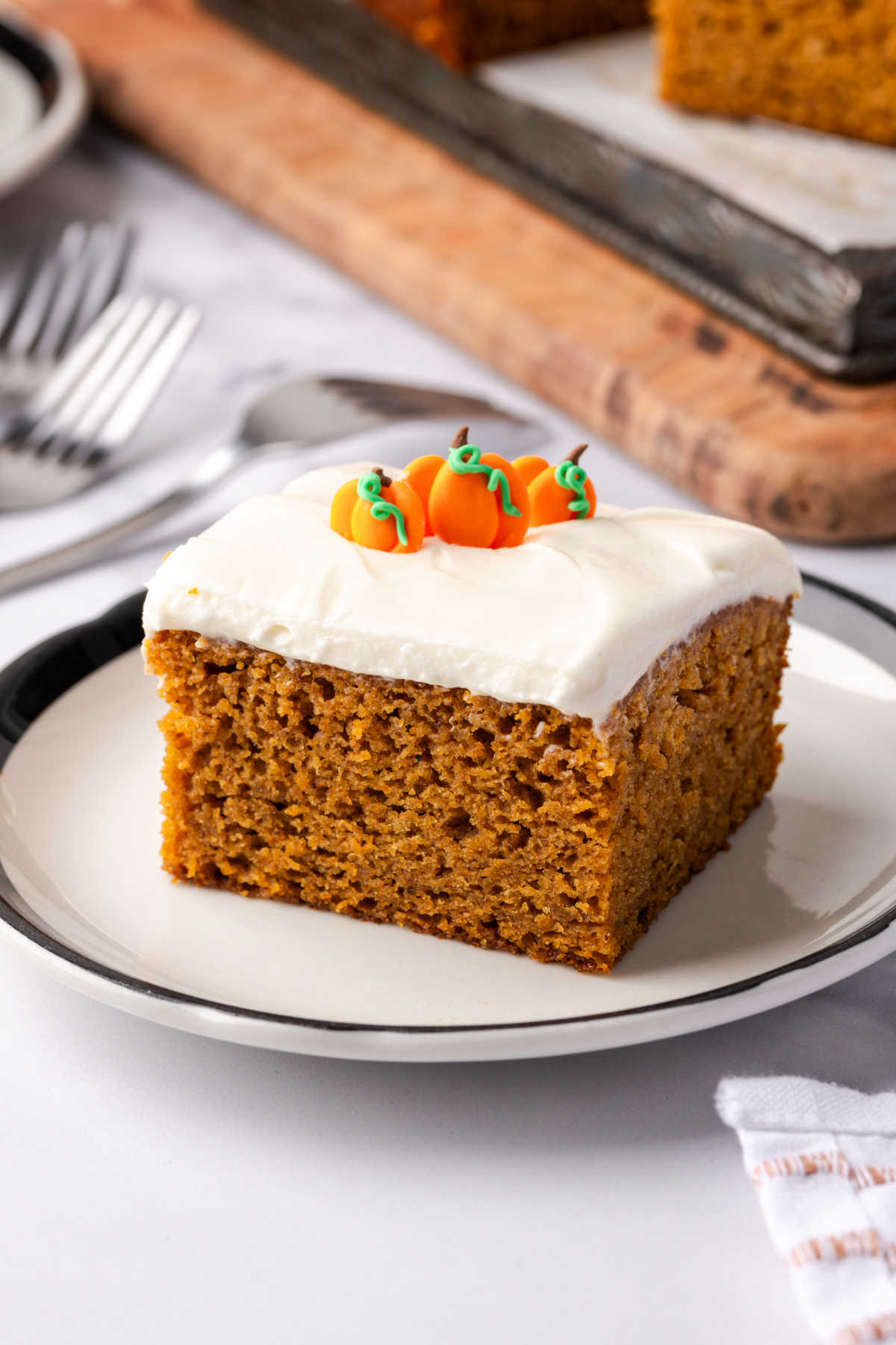 Pumpkin cake square with frosting, pumpkin candies on small white plate.