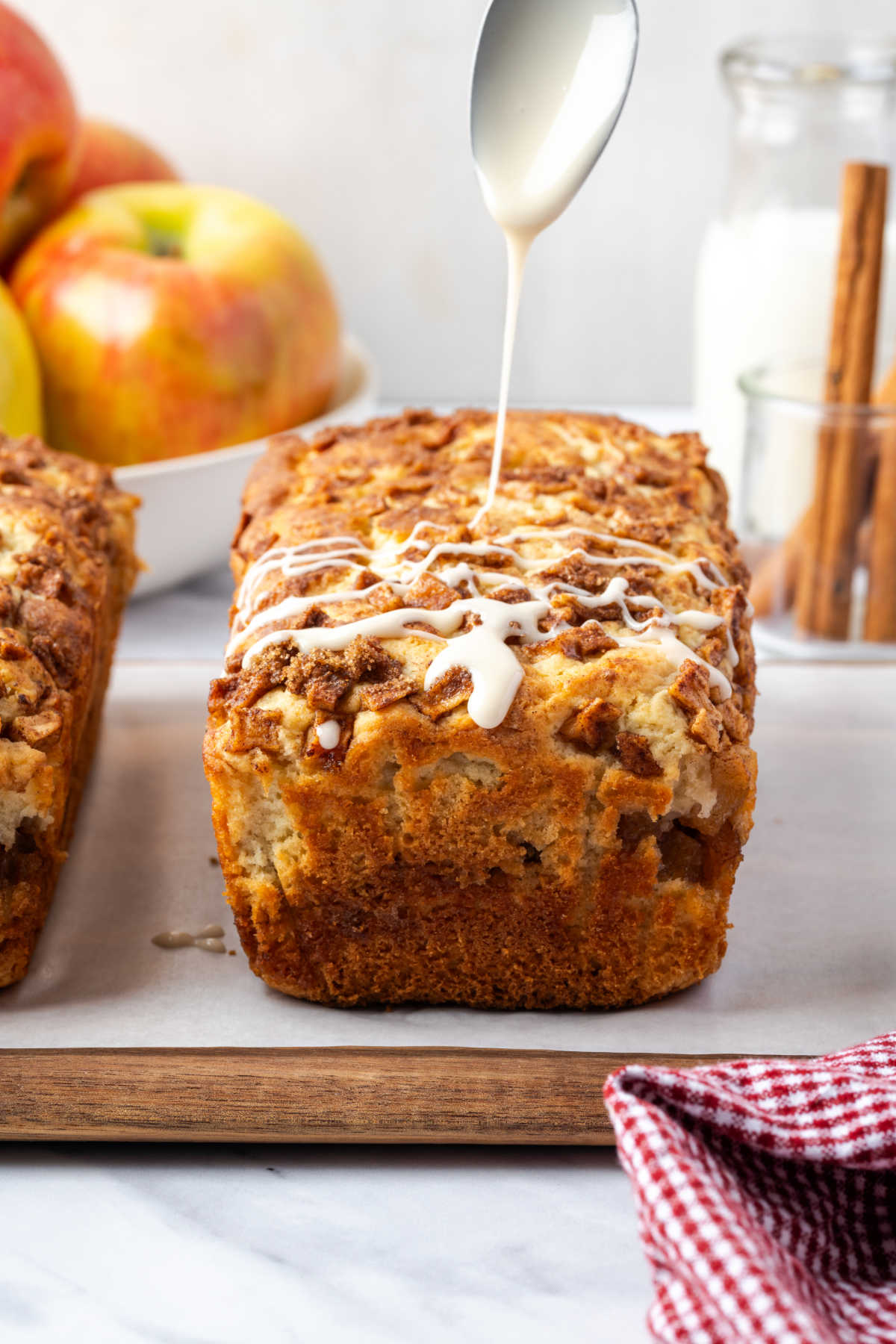 Spoon adding icing on apple loaf cake on wood cutting board.