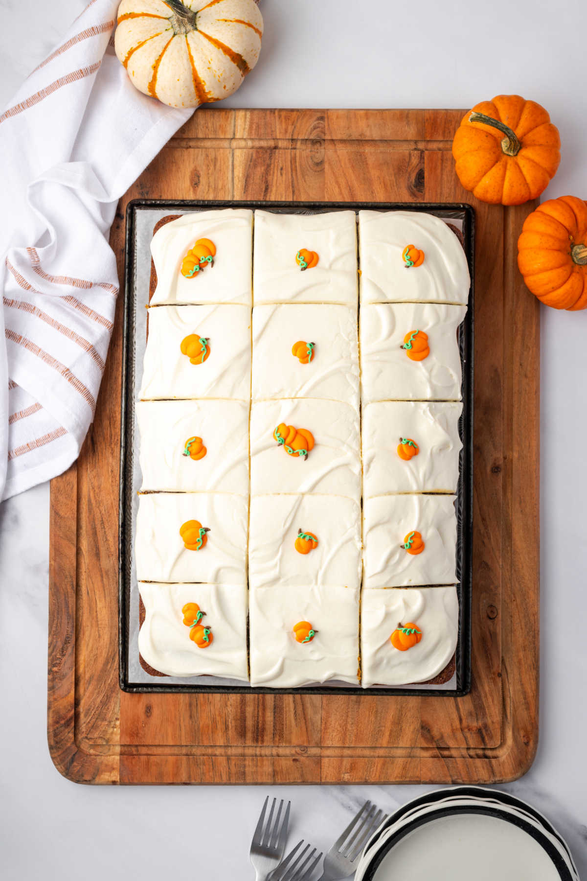Pumpkin cake cut into squares with pumpkin candies on wood cutting board.